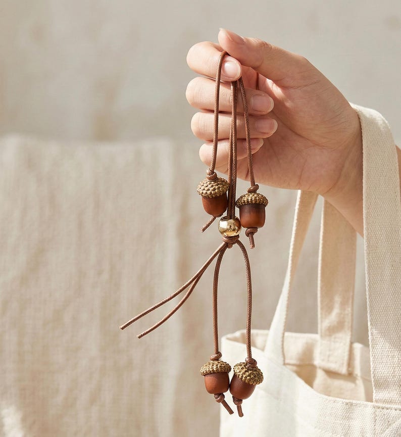 May include: A brown acorn pendant with four acorn charms. The acorn caps are a light brown color, and the acorn bodies are a darker brown. A gold-colored bead is at the center of the pendant.