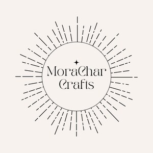 May include: A circular logo with the text "MoraChar Crafts" in a stylized font, surrounded by radiating lines. A small star is above the "a" in "Char". The design is in black on a cream-colored background.