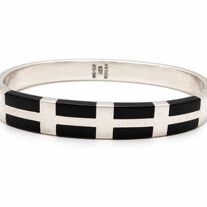 Op de afbeelding: Een zilverkleurige armband met een geometrisch ontwerp. De armband heeft afwisselende secties van gepolijst zilver en zwarte rechthoekige inlays. De tekst "MEXICO 925" is aan de binnenkant van de armband gestempeld.