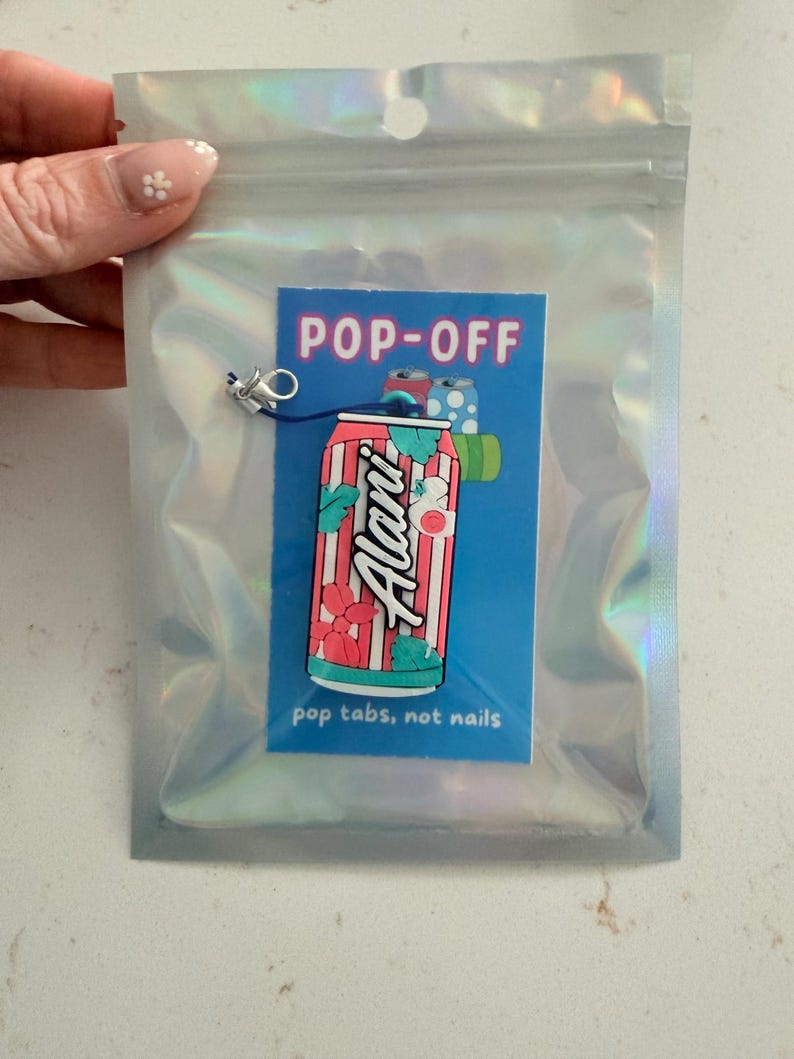 May include: A colorful Alani Nu soda can design on a blue background with the text "POP-OFF" and "pop tabs, not nails." The design is in a holographic bag with a small charm attached.