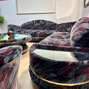 May include: A vintage living room set featuring a sofa, two armchairs, and a coffee table. The furniture has a unique design with a velvet fabric in shades of burgundy, teal, and gray. The coffee table and armchairs have mirrored tops and gold trim.