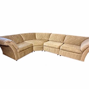 May include: A large, beige sectional sofa featuring a modular design with multiple seating sections. The upholstery has a quilted, diagonal stitched pattern across the back cushions and armrests, with smooth, plush seat cushions and rounded arms.