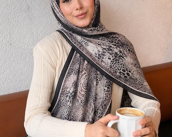 Op de afbeelding: Een crèmekleurige, geribbelde top met lange mouwen gecombineerd met een zwart-grijze hijab met dierenprint en een effen zwarte rand. De hoofddoek heeft een gedetailleerd patroon van luipaardvlekken en zebrastrepen, elegant gedrapeerd over de schouders.