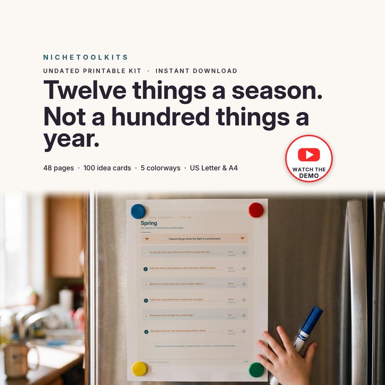 Op de afbeelding: Een printbare set met de titel Twelve things a season. Not a hundred things a year. Het document bevat een lentelijst met genummerde items, selectievakjes en lijnen om op te schrijven. Het is met vier gekleurde magneten aan de koelkast bevestigd.