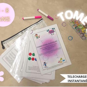 Peut inclure: Un ensemble de fiches d'activités éducatives intitulé CONNEXIONS MAGIQUES : DÉFIS PHYSIQUES ET JEUX POUR RÉVEILLER MON CERVEAU TOME 2, avec des illustrations colorées, une trousse transparente, deux feutres et une boîte d'anneaux en plastique.