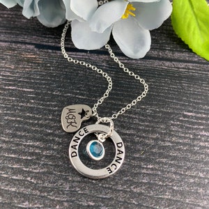 Puede incluir: Collar de plata con un dije de piedra azul y dos dijes de plata. Uno es un corazón con la palabra "Love" y una estrella. El otro es un círculo con la palabra "Dance" escrita dos veces.