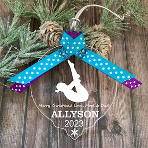 May include: A clear acrylic Christmas ornament featuring a silhouette of a gymnast in a handstand pose. The ornament is decorated with a teal and purple ribbon with white polka dots. The text "Merry Christmas! Love, Mom & Dad" and "ALLYSON 2023" is printed on the ornament.