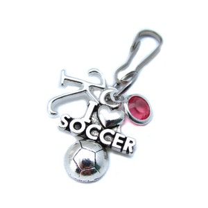 May include: Silver charm with a soccer ball, a heart with a red rhinestone, and the words "I love soccer".