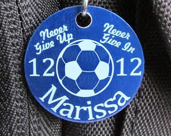 May include: Blue round tag with a white soccer ball and the text "Never Give Up 12 Never Give In 12 Marissa"