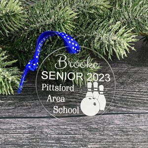 May include: A clear round Christmas ornament with the text "Brooke Senior 2023 Pittsford Area School" and a bowling ball and pins graphic.