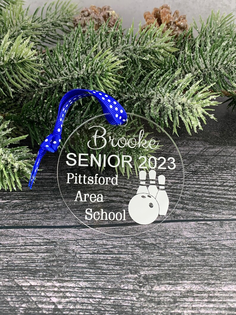 May include: A clear round Christmas ornament with the text "Brooke Senior 2023 Pittsford Area School" and a bowling ball and pins graphic.
