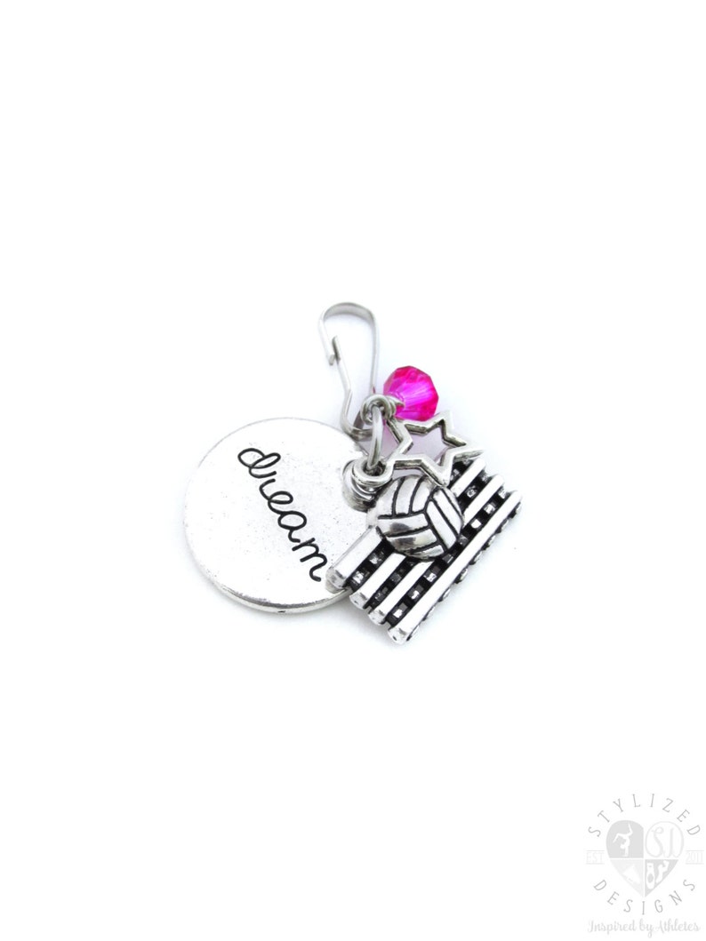 May include: Silver charm with a volleyball, a star, and a pink bead. The charm has the word "dream" engraved on a round disc.