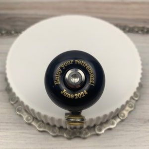May include: Black bicycle bell with gold lettering that reads "Enjoy your retirement! June 2024".