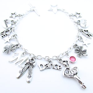 Puede incluir: Pulsera de plata con varios charms, incluyendo una bailarina, un trébol de cuatro hojas, una estrella, un corazón y las palabras "Believe" y "Love".
