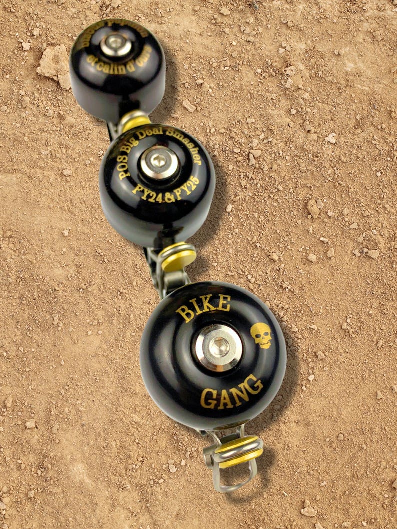 May include: Three black bike bells with gold lettering. The top bell says "Pos Big Deal Smasher FY24 & FY25". The middle bell says "Bike Gang" with a skull graphic.