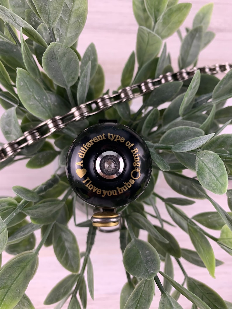May include: A black bicycle bell with a gold inscription that reads "A different type of ring. I love you bubs."
