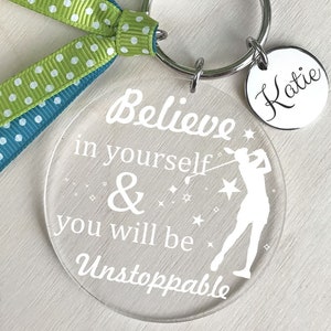 May include: A clear acrylic keychain with the text "Believe in yourself & you will be Unstoppable" and a silhouette of a golfer. The keychain also includes a silver charm with the name "Katie" written on it.