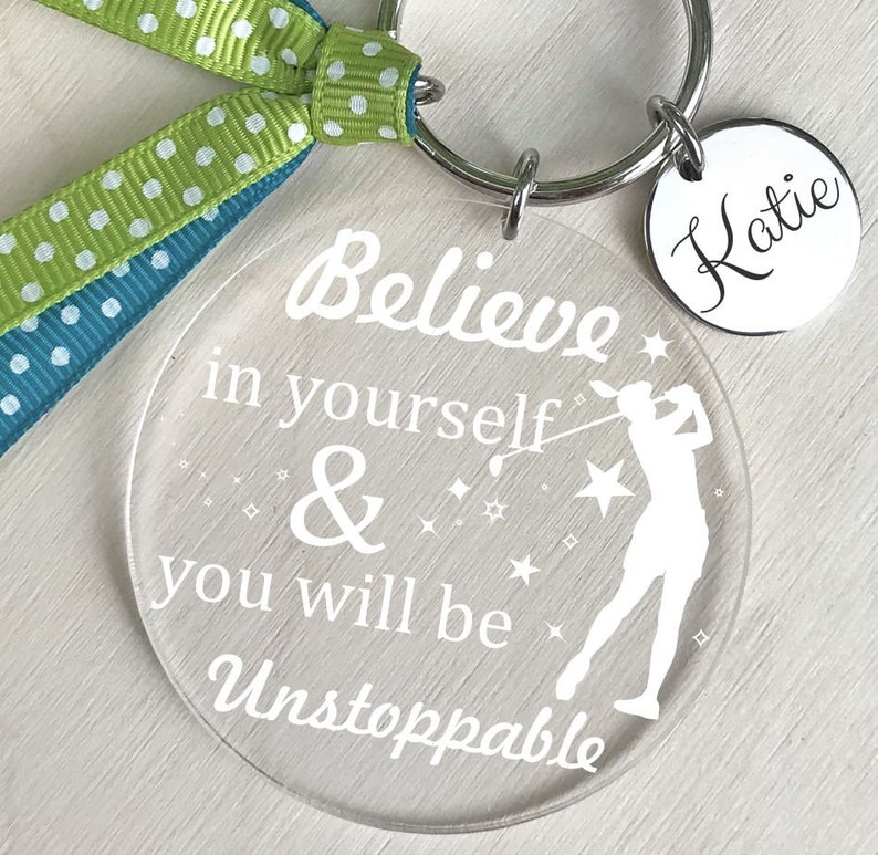 May include: A clear acrylic keychain with the text "Believe in yourself & you will be Unstoppable" and a silhouette of a golfer. The keychain also includes a silver charm with the name "Katie" written on it.