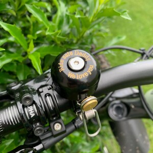 May include: Black bicycle bell with a gold inscription that reads "Ride Safe Daddy We Love You".