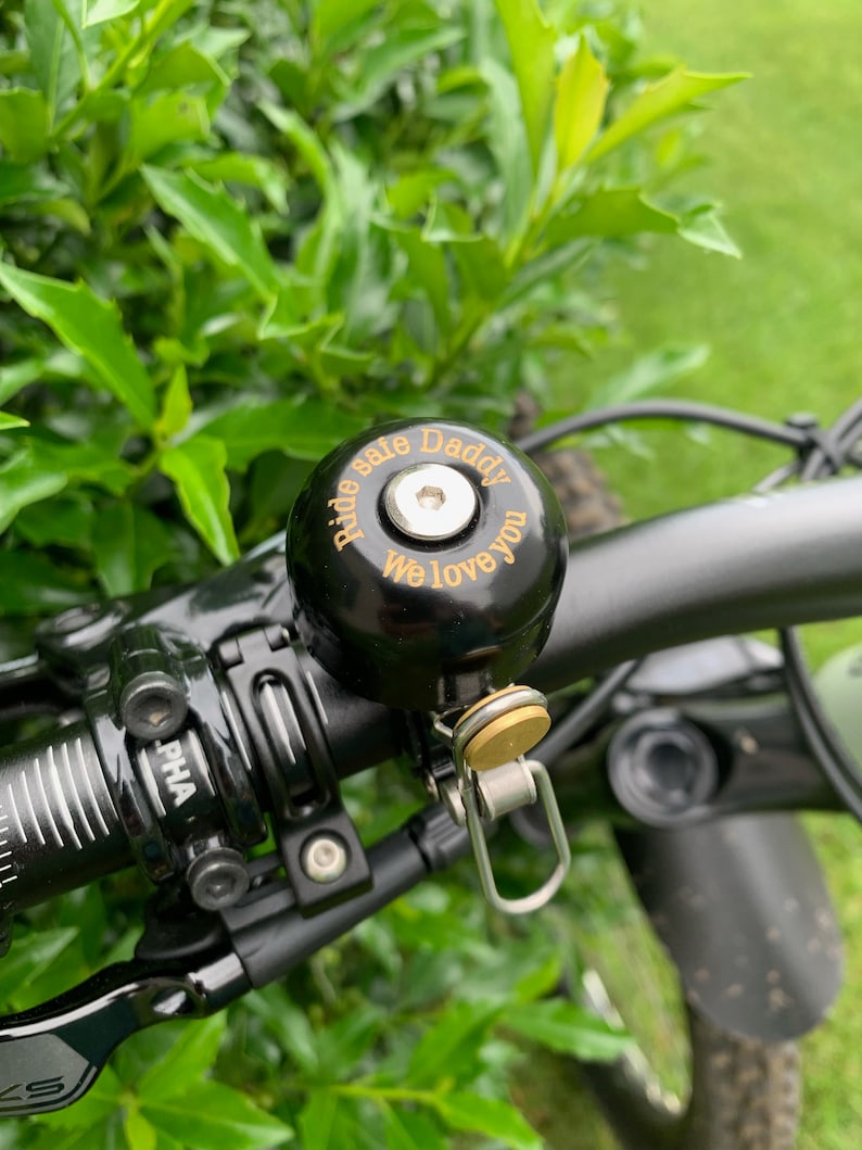May include: Black bicycle bell with a gold inscription that reads "Ride Safe Daddy We Love You".
