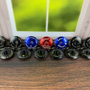 May include: Ten personalized bike stem caps with various colors and engraved messages. The caps are black, blue, red, and silver. The messages include "This Dad Shreds", "We love you, Daddy", "#1 Dad and Bike Legend", "Send it! I love you Charlotte", "Love You Always", "Go Daddy Go! Shred the Gear", "Daddy Shreds Love Maude", "We love you Chiannon & Wesley", "Pedal faster Love Evy", "Papa We Love You!"