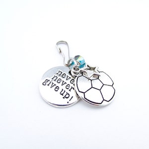 May include: Silver charm with a soccer ball design and a round charm with the text "never never give up!"