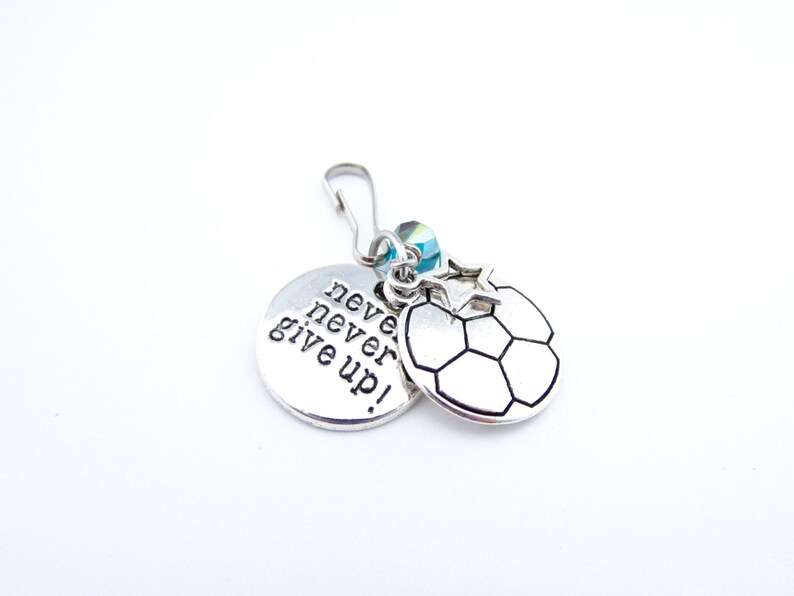 May include: Silver charm with a soccer ball design and a round charm with the text "never never give up!"
