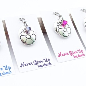 May include: Four silver soccer ball bag charms with different colored crystals. Each charm has the text "Never Give Up" and "bag charm" printed on a white card.