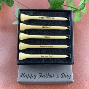 May include: A set of five wooden golf tees in a black box. The tees are engraved with messages for Father's Day, including "Happy Father's Day!" "Golf Dad" "#1 DAD" "Best Dad by Par" and "Nice shot, Dad!" The box is also engraved with the text "Happy Father's Day".