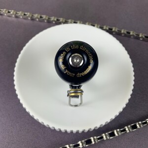 May include: Black bicycle bell with a gold inscription that reads "Ride in the direction of your dreams".