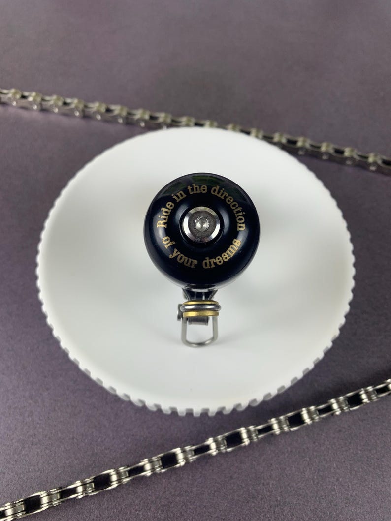 May include: Black bicycle bell with a gold inscription that reads "Ride in the direction of your dreams".