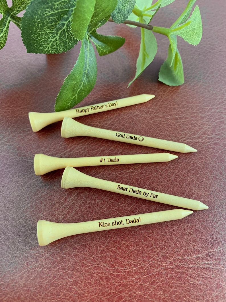 May include: Four wooden golf tees with personalized messages. The messages include "Happy Father's Day!", "Golf Dada", "#1 Dada", "Best Dada by Par", and "Nice shot, Dada!"