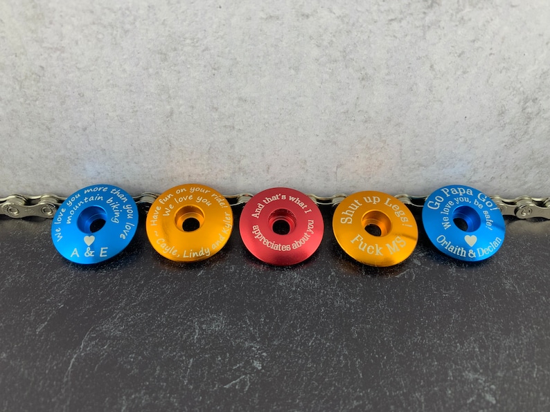 May include: Five different colored metal bike stem caps with personalized engravings. The engravings include messages of love, appreciation, and humor.