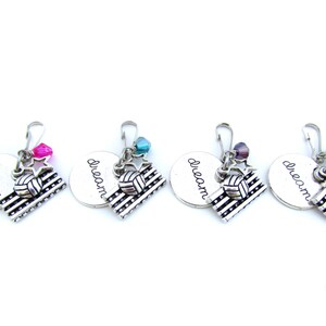 May include: Four silver zipper pulls with a volleyball and the word "dream" engraved on them. Each pull has a different colored star charm.
