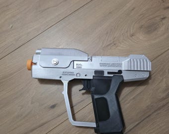 Könnte beinhalten: Eine silberne und schwarze Spielzeugpistole mit einer orangefarbenen Spitze am Lauf. An der Seite des Rahmens steht der Text "MA 2552" und "MISRIAH ARMORY 12.7MM AUTOMATIC" sowie "SUP SPACE PREPSTANCE". Sie hat einen schwarzen Griff und ein abnehmbares Magazin.