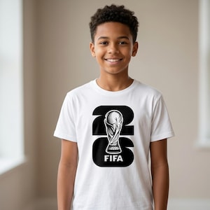 以下が含まれることがあります： FIFAワールドカップのトロフィーと数字22の白黒グラフィックが特徴の白いTシャツ。トロフィーの下には「FIFA」の文字がプリントされています。笑顔の人が着ています。