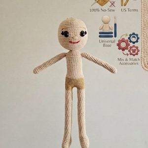 May include: A crocheted doll with a neutral skin tone, featuring a smiling face with black eyes and a red mouth. The doll has outstretched arms and is wearing a pair of tan shorts. The image also includes text that says "100% No-Sew", "US Terms", "Universal Base", and "Mix & Match Accessories".