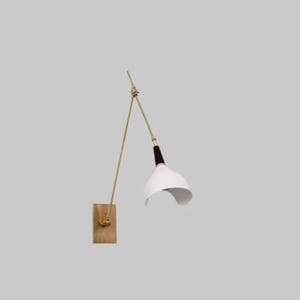 May include: A modern wall-mounted lamp with a white lampshade and a black accent. The lamp features a brass-colored arm and a wooden base. The design is minimalist and stylish, suitable for various interior styles.
