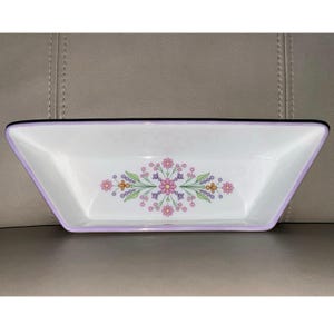 May include: A rectangular white ceramic serving dish with a floral design in the center. The dish has a lavender rim and a dark purple border. The floral pattern includes pink, orange, and green elements.
