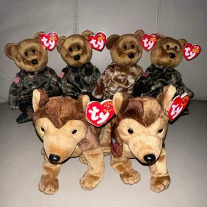 Pode incluir: Uma coleção de brinquedos de pelúcia com ursos marrons em trajes de camuflagem e cães marrons e castanhos. Cada brinquedo tem uma etiqueta vermelha em forma de coração. Os ursos e os cães estão dispostos em grupo.