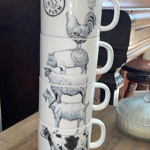 May include: A stack of four white ceramic mugs with black and white farm animal illustrations. The top mug has the text "FARM SWEET FARM" and a rooster design. Other mugs feature a pig, sheep, goat, and cow.