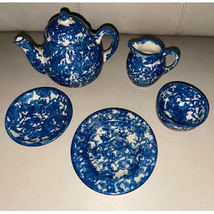 May include: A tea set comprising a teapot with a lid, a creamer jug, two small plates, and a bowl. Every item features a blue and white mottled sponge-painted pattern, ensuring a uniform appearance across the entire ceramic tea service collection.