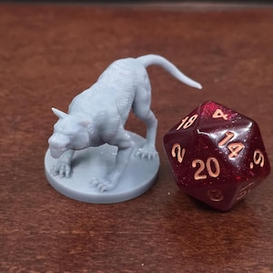 May include: A light grey miniature wolf figurine and a red, multi-sided die with white numbering. The die shows the number 20. The wolf is on a circular base.