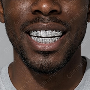 Puede incluir: Un conjunto de parrillas dentales plateadas que cubren los dientes superiores e inferiores, con un engaste pavé denso de pequeñas piedras claras y reflectantes. La palabra Glimmersmile se repite como marca de agua en la imagen.