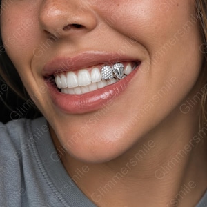 Puede incluir: Un conjunto de grillz plateados para dos dientes superiores. Una funda dental es rectangular y está totalmente incrustada con pequeñas piedras claras, mientras que la funda adyacente es triangular y presenta un acabado metálico liso y puntiagudo.