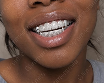 May include: A set of silver-toned dental grills covering the upper and lower teeth, featuring a dense pavé of small, clear, reflective stones. The design includes pointed, fang-like caps on the outer edges of the upper and lower teeth rows.