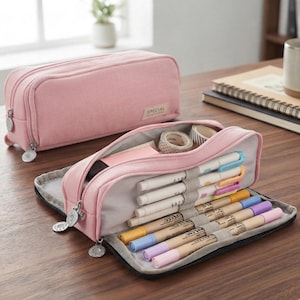 May include: Two light pink rectangular pencil cases made of fabric. One case is closed, and the other is open, revealing internal elastic loops holding several colored pens and markers, along with a small roll of adhesive tape inside the main compartment.