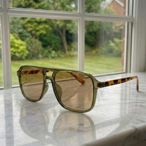 May include: Aviator sunglasses featuring a translucent olive green frame and a double bridge design. The temples display a brown and black tortoiseshell pattern, while the lenses are tinted in a warm, light brown hue, providing a clear view.