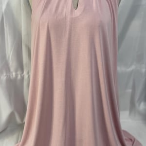 May include: A sleeveless, pale pink dress with a keyhole neckline. The dress is displayed on a mannequin, showcasing its flowing, floor-length design. The fabric appears soft and drapes elegantly, suggesting a comfortable fit. The overall style is simple and chic.
