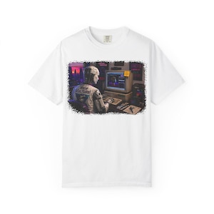May include: White t-shirt featuring a retro-style graphic of a person at a vintage computer. The graphic includes a cityscape, a computer monitor, and the text "RICH VULTURE" on the person's jacket. The design has a pixelated, digital art aesthetic.